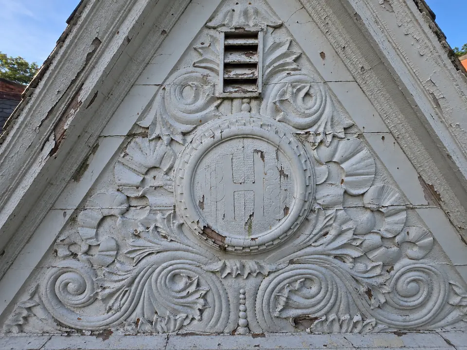 The Harris crest before restoration, with peeling white paint over the carved H and date.