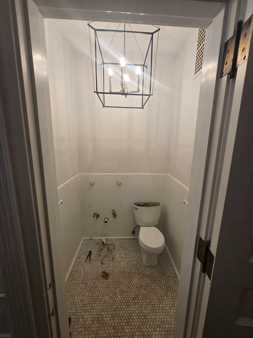 The powder room before, with white walls and tile, a hexagon tile floor, a cage-style light and the sink removed.