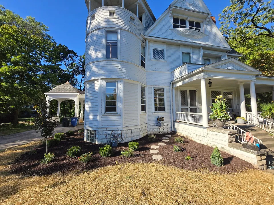 The tower side of the house with new mulched beds, young shrubs, a stepping-stone path and straw over the newly seeded lawn.
